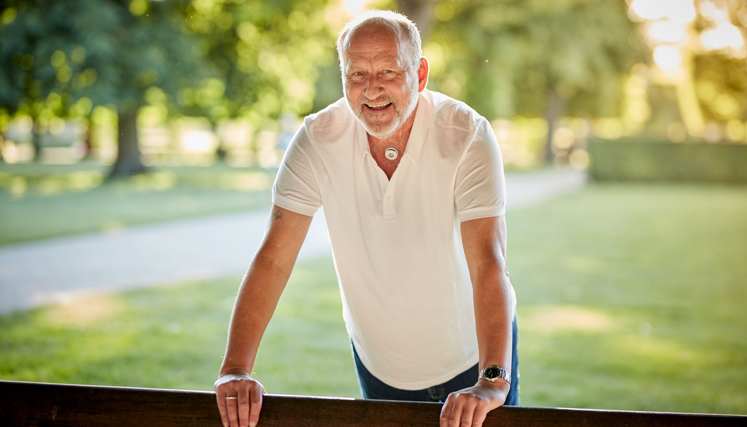 Laryngektomierter Mann mit einem HME genießt einen sonnigen Tag im Park